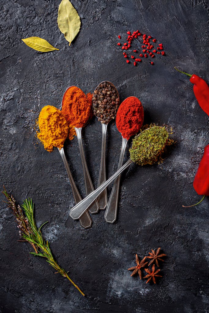 An artistic flat lay of colorful spices on a dark textured surface.