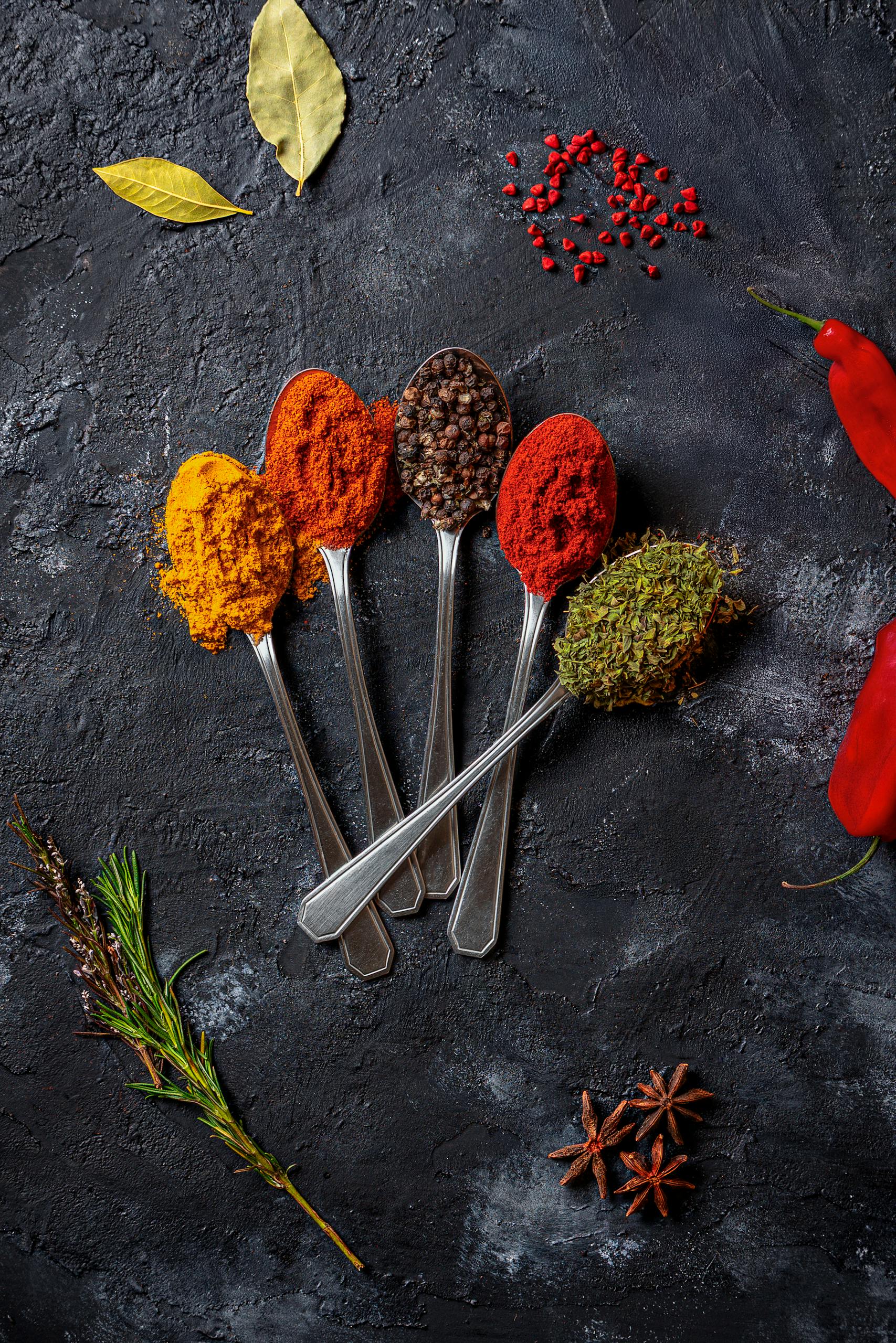 An artistic flat lay of colorful spices on a dark textured surface.