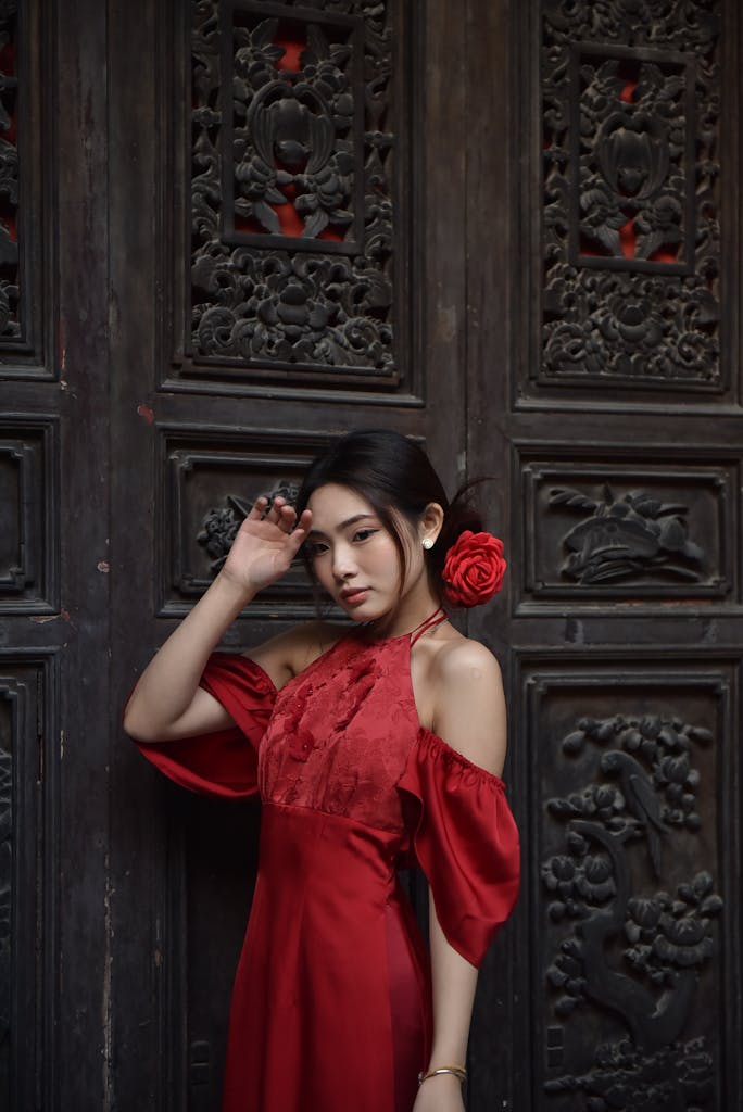 Woman in an elegant red dress standing against an ornately carved wooden door.